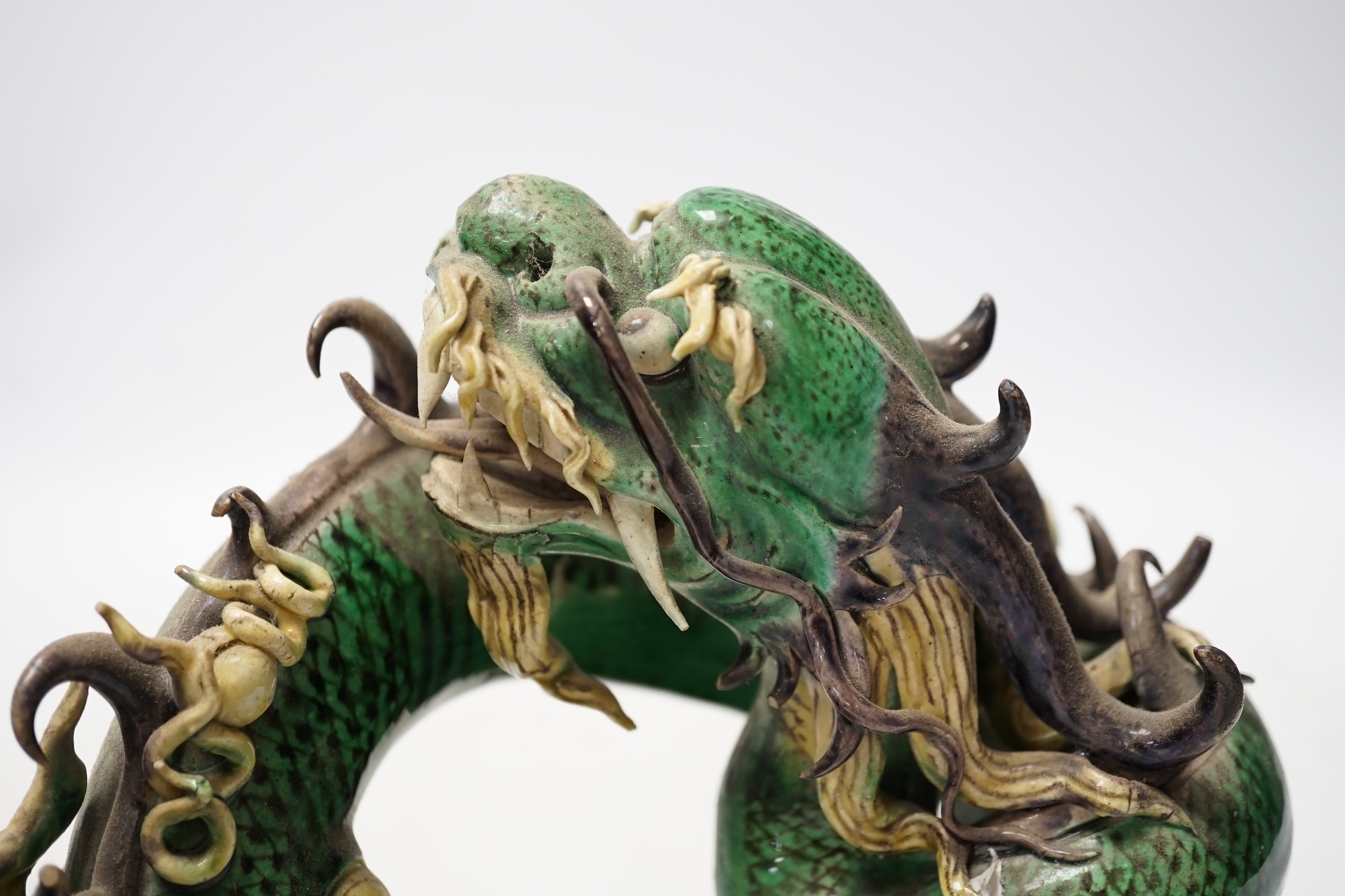 A Chinese sancai glazed model of a dragon, silk covered stand, 28cm wide. Condition - some damage